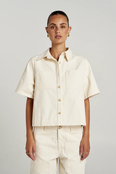 Front studio shot of a model wearing the cropped Summi Summi Carpenter SS Shirt in Ecru, highlighting the pointed collar, button-down front, and dual chest patch pockets.