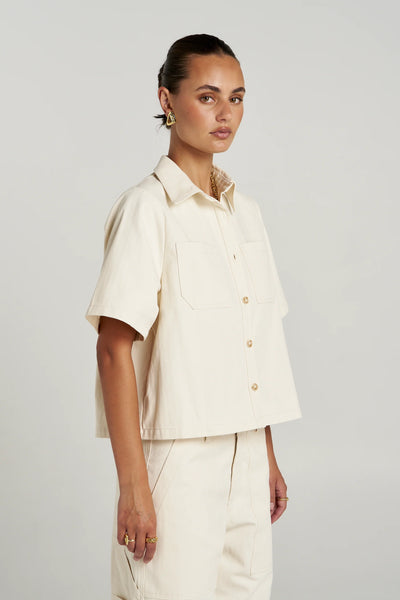 Three-quarter profile view of a model in the short-sleeve Summi Summi Carpenter SS Shirt in Ecru cotton herringbone twill.