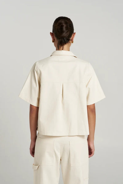 Back view of a model wearing the boxy Summi Summi Carpenter SS Shirt in Ecru showing the back yoke and center pleat detail.