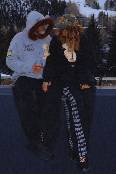 A full-length shot from the front on a model wearing the cream-colored oversized hoodie, highlighting the loose streetwear silhouette, drop shoulders, spacious front kangaroo pocket, ribbed cuffs, and thick adjustable drawstring hood cords.