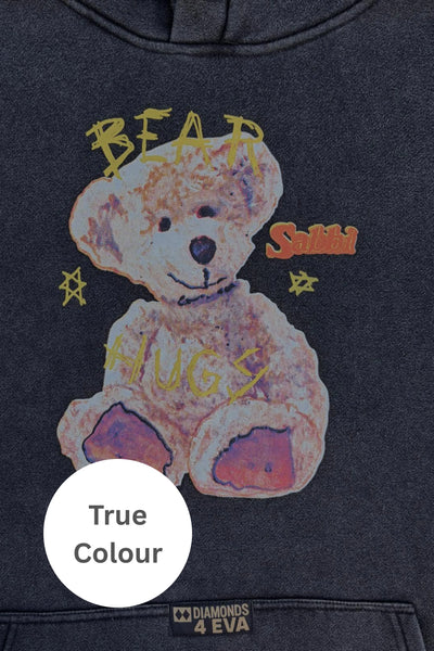 A clean flat-lay product photograph of the Gimme Bear Hugs Hoodie displayed flat against a solid white background, showcasing the off-white cream colorway, its heavy fleece fabrication texture, relaxed slouchy sleeves, and the signature illustrated teddy bear graphic printed on the center chest.