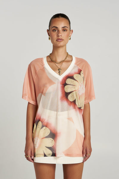 Studio front view of a model wearing the sheer Summi Summi Harlequin Tee in Harlequin print with a white V-neckline and short raglan sleeves.