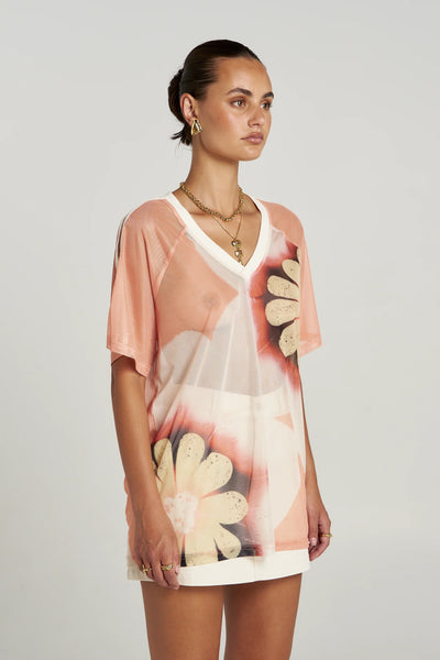 Three-quarter front view of a model in the relaxed-fit Summi Summi Harlequin Tee, styled with gold layered necklaces and a white mini skirt.