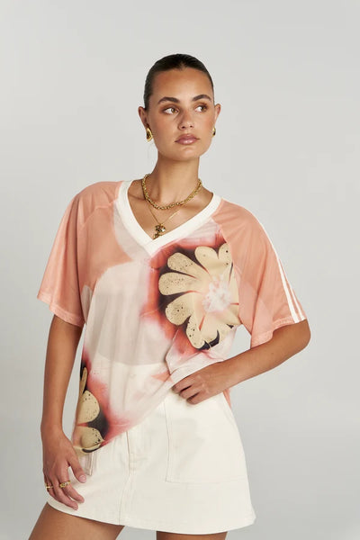 Mid-shot close-up of a model posing in the sheer floral-print Summi Summi Harlequin Tee with a hand resting on her waist.