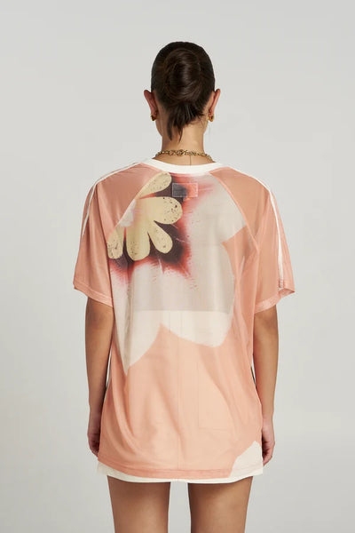 Back view of a model wearing the semi-sheer Summi Summi Harlequin Tee featuring a large peach and floral print with raglan sleeve stitching.