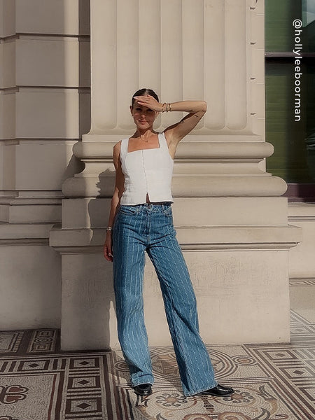 Full-length outdoor outfit shot of model wearing Senso Cooper III black leather loafers, paired with pinstripe wide-leg jeans and a white square-neck corset top.