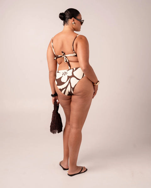 An over-the-shoulder lifestyle image focusing on the back of the Ibisco tie-back balconette top, clearly detailing the functional fabric tie closure, thin adjustable straps, and the premium ribbed texture of the cream and neutral brown abstract floral fabric.