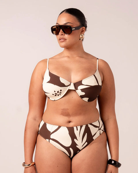 A three-quarter view lifestyle shot of a model posing outdoors in the Ochre Lane Ibisco balconette bikini top, displaying the comfortable side support and full coverage provided by the wide-set underwire cups.