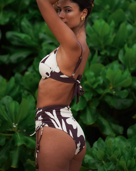 A front-facing lifestyle shot of a model standing against vibrant green foliage, showcasing how the Ibisco underwire bralette offers lift and shape-enhancing definition for D-cup and above silhouettes.