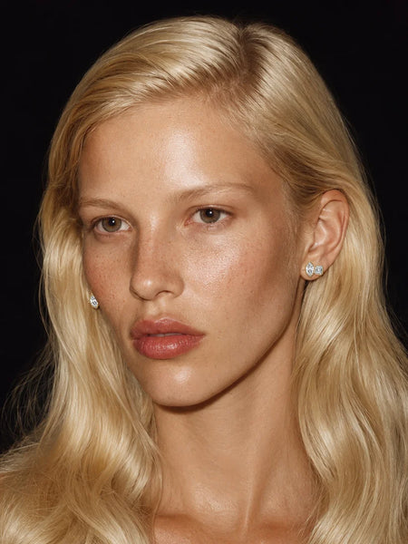 Close-up portrait of a model with blonde hair wearing the Avant Studio Marguerite Stud Earrings in gold, featuring a bezel-set marquise-cut and emerald-cut stone.