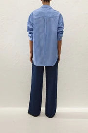 Back view of a model wearing the Faithfull The Brand En Vau Shirt in Joao Stripe Azulejo Blue, paired with dark blue wide-leg jeans, highlighting the dropped shoulders and curved back hem.