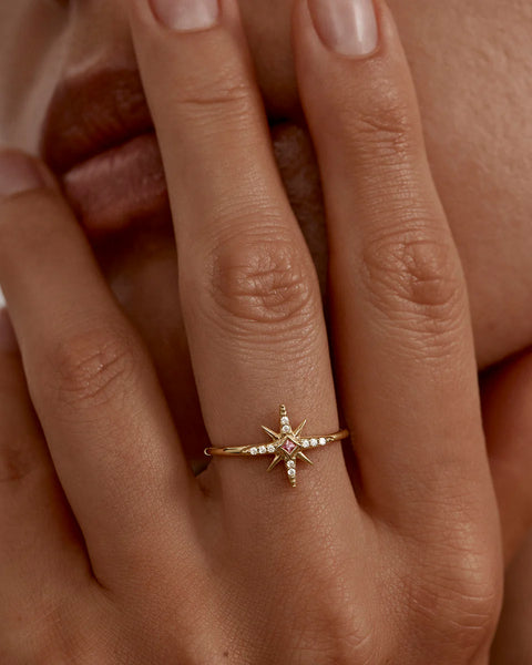 18k gold star-shaped ring with a pink gemstone on a hand.