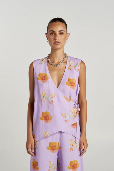 Front portrait view of a model wearing the sleeveless Summi Summi Tie Front Vest in Reverie, featuring a deep V-neckline, wrap silhouette, and side tie closure in lilac floral-butterfly print linen blend.