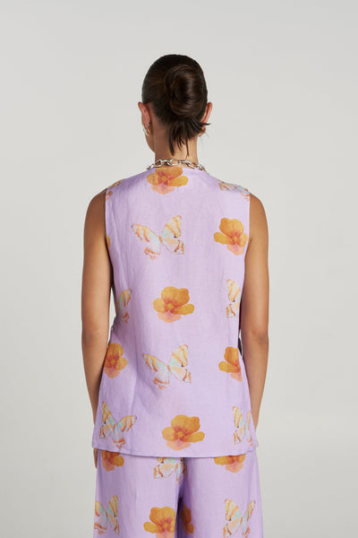Back view of a model wearing the sleeveless Summi Summi Tie Front Vest in Reverie showing the straight hemline and vibrant butterfly floral print pattern.