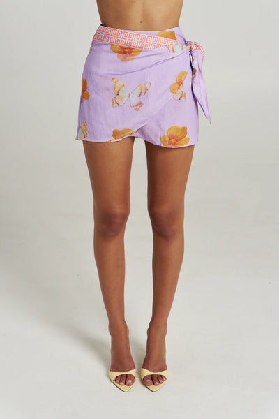 Front studio shot of the high-waisted Summi Summi Wrap Skirt in Reverie mini length, featuring a side tie closure and patterned waistband in lilac linen-rayon blend.