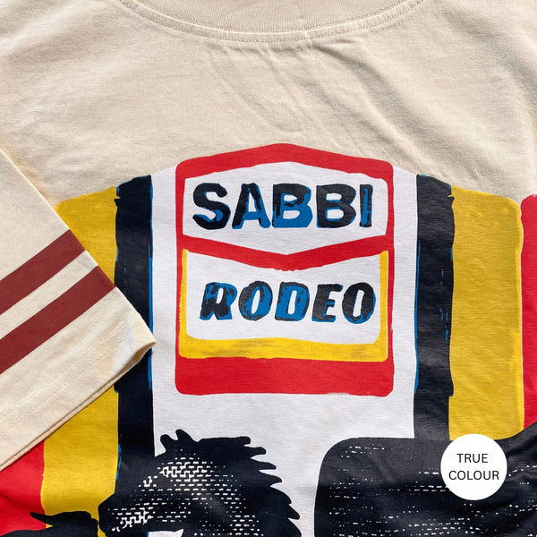 A flat-lay studio product photograph of the Very Oversized Sabbi Rodeo Self Love Club Tee in beige, displayed flat against a neutral backdrop to highlight its square, relaxed silhouette, relaxed crewneck, and the colorful, old-school garage-style graphic text printed on the front.