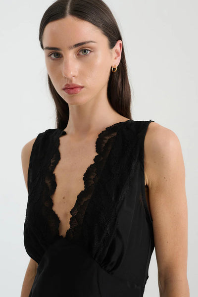 Close-up studio view of a dark-haired model wearing the ROWIE Annie Silk Mini Dress in Noir, highlighting the delicate hand-cut scalloped lace trim along the deep V-neckline.