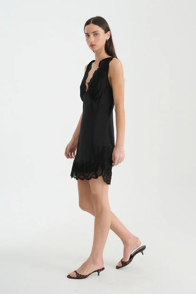Three-quarter side shot of a model walking in the ROWIE Annie Silk Mini Dress in Noir, showing the soft side split and vintage-inspired bias-cut silhouette.