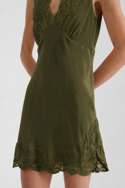 Close-up studio view of the ROWIE Annie Silk Mini Dress in Olive, showcasing the intricate hand-cut olive lace trim along the deep V-neckline, side split, and scalloped hemline.