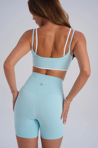Studio rear view from the waist to upper thigh showcasing high-waisted ice blue squat-proof bike shorts with a subtle silver circular logo on the back waistband.