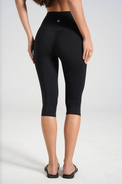 Lower body rear three-quarter view showing the back waistband contouring and 3/4 capri length cut of black activewear leggings.