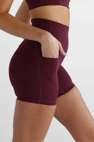 Close-up side profile view of a model sliding her hand into the large side phone pocket of high-waisted cherry cola bike shorts.