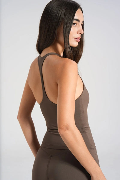 Studio rear three-quarter view of a model showing the slim T-back racerback strap design of a dark chocolate brown athletic tank top.