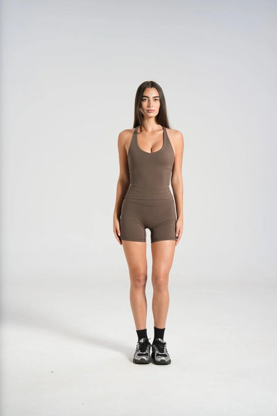 Full-length studio front view of a model wearing a dark chocolate brown slim-fit scoop-neck activewear tank top with built-in shelf bra, paired with matching bike shorts and sneakers.