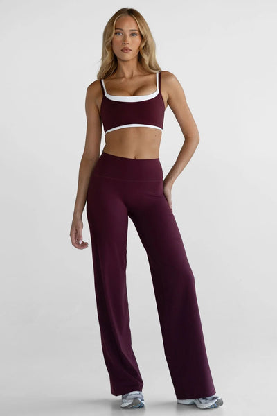 Full-length front view of a model wearing the high-waisted, wide-leg Leelo Sculpt Pants in Cherry Cola with a matching sports bra.