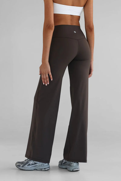 Rear view studio shot from the waist down of a model wearing the LEELO Tall Sculpt Wide Leg Pants in dark chocolate brown. The image highlights the high-waisted seamless waistband, smooth performance fabric construction, and a small silver silicone logo centered on the back of the waistband.
