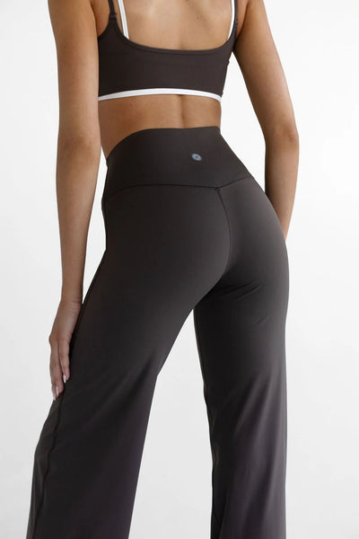 A close-up rear studio shot highlighting the upper fit of the LEELO Tall Sculpt Wide Leg Pants in dark chocolate brown. The focus shows the subtle V-shaped seam detail at the back, the small silver branding mark, and the clean stitch lines of the premium activewear fabric.