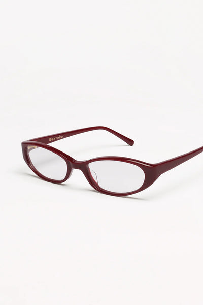 Three-quarter product view of the SHEVOKE Silon maroon oval-rectangular glasses highlighting gold inner temple logo branding and clear lenses.