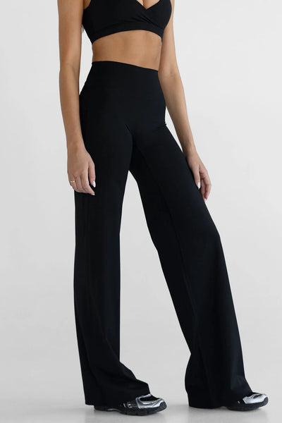 A mid-length studio lifestyle shot of a model facing forward, demonstrating how the versatile black high-waisted sculpt pants cross over from a yoga or Pilates workout to comfortable everyday lounging.